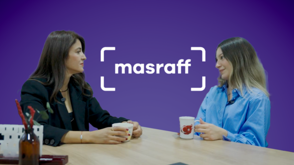 Mor arka plan üzerinde Masraff logosu önünde, masa başında karşılıklı kahve içerek röportaj yapan iki kadın profesyonel.